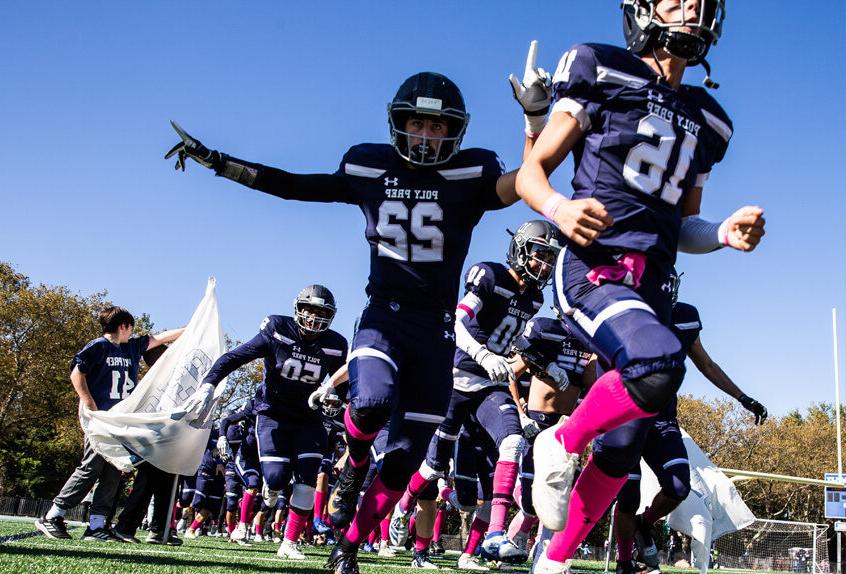 Poly Prep Varsity Football Team breaking through a banner at the Homecoming game